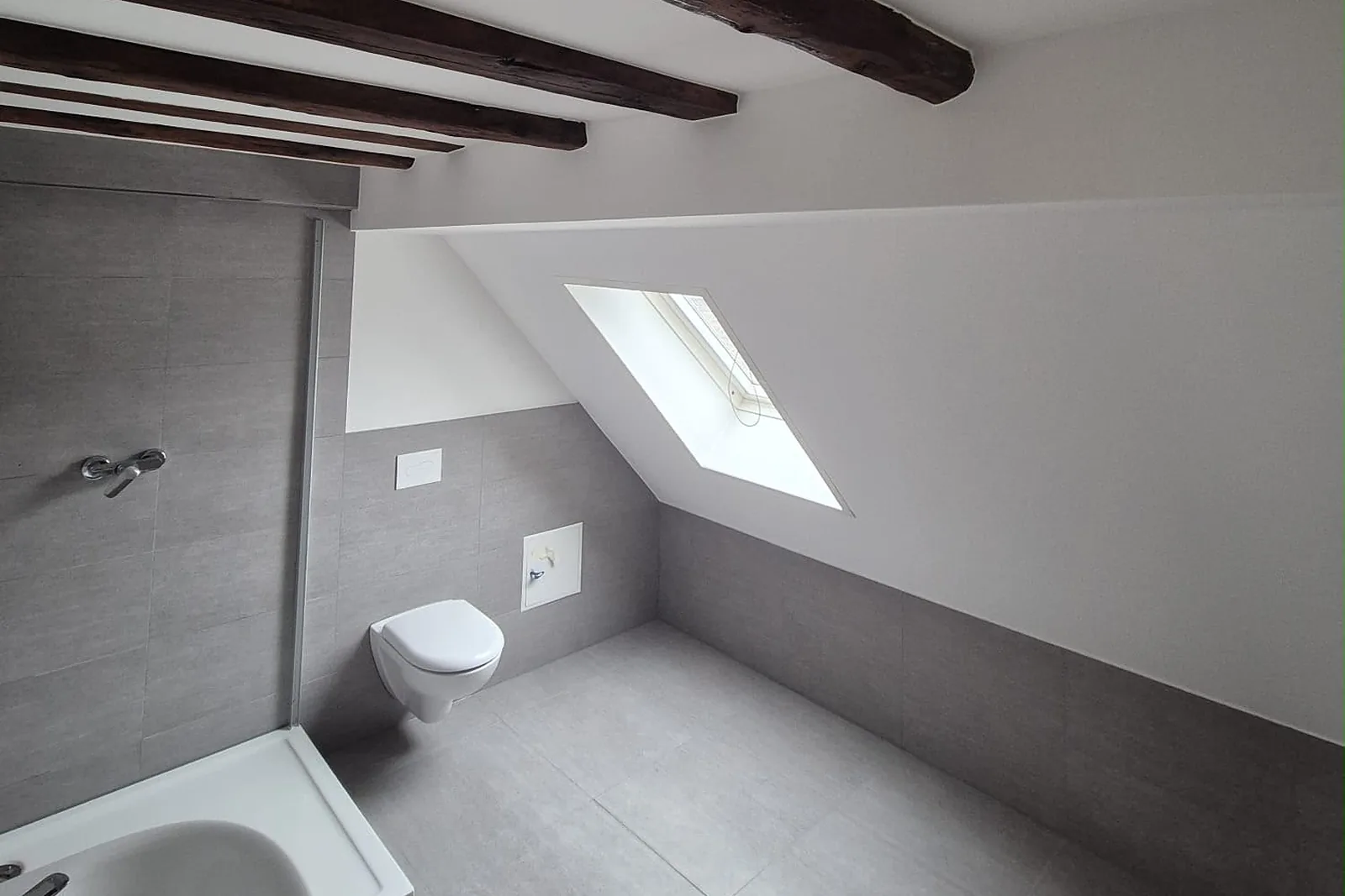 Dachgeschossbad mit Dachfenster in der Schräge, Wand-WC und dunklen Deckenbalken