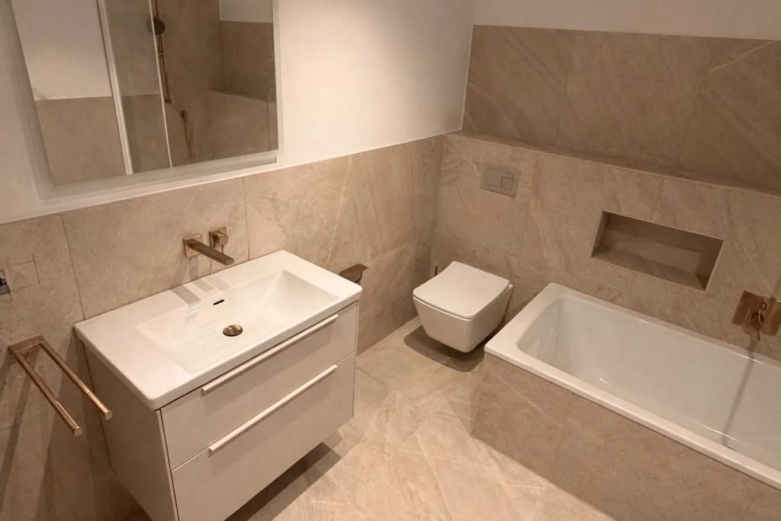 Bad mit großformatigen Fliesen in heller Steinoptik, Waschtisch mit Unterschrank, Wand-WC und Badewanne