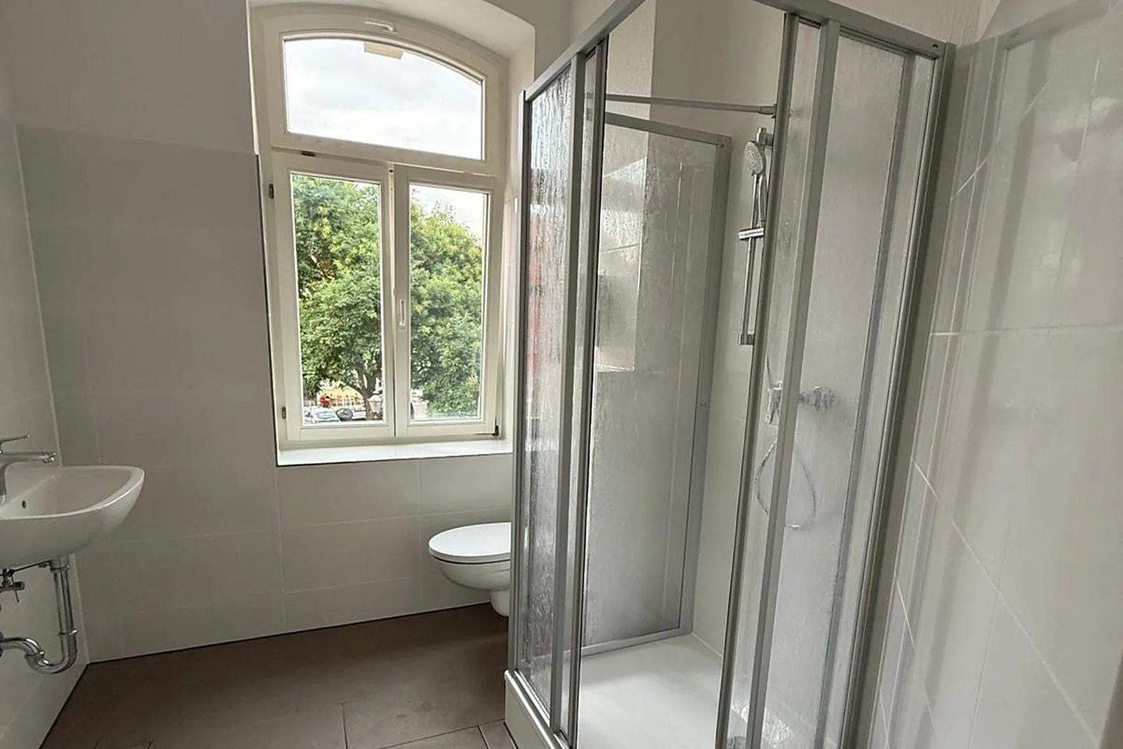 Saniertes Altbaubad mit Bogenfenster, Duschkabine, kleinem Waschbecken und Wand-WC
