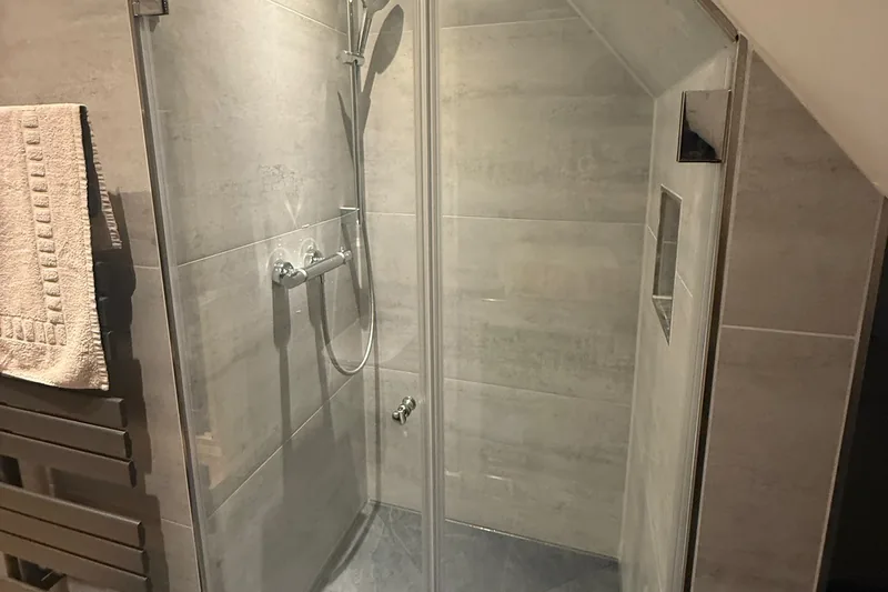 Duschabtrennung: Dusche unter der Dachschräge hinter Klarglastüren, seitlich eine eingeflieste Nische